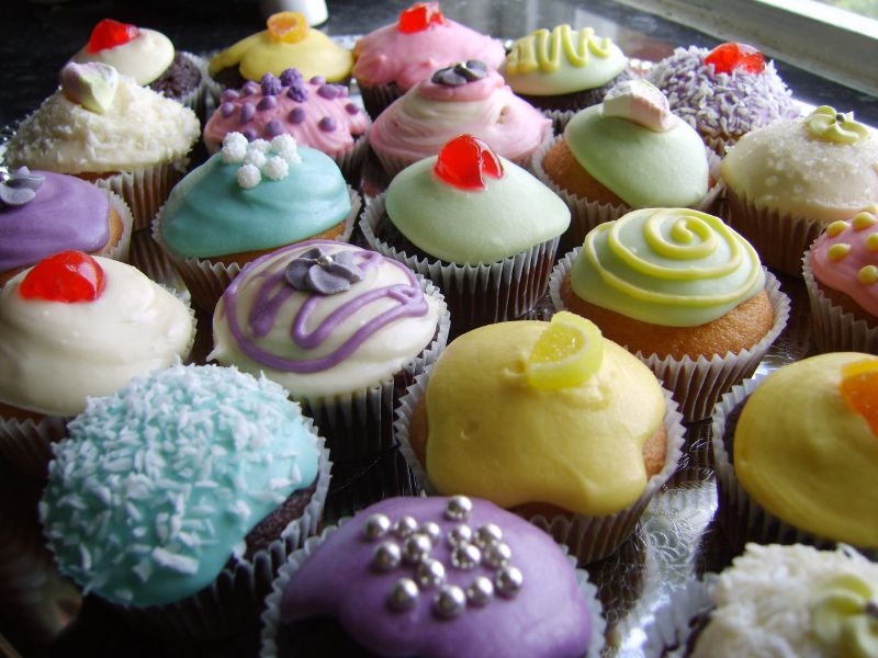 A photo of a batch of cupcakes with pastel colored frosting and edible decorations on top